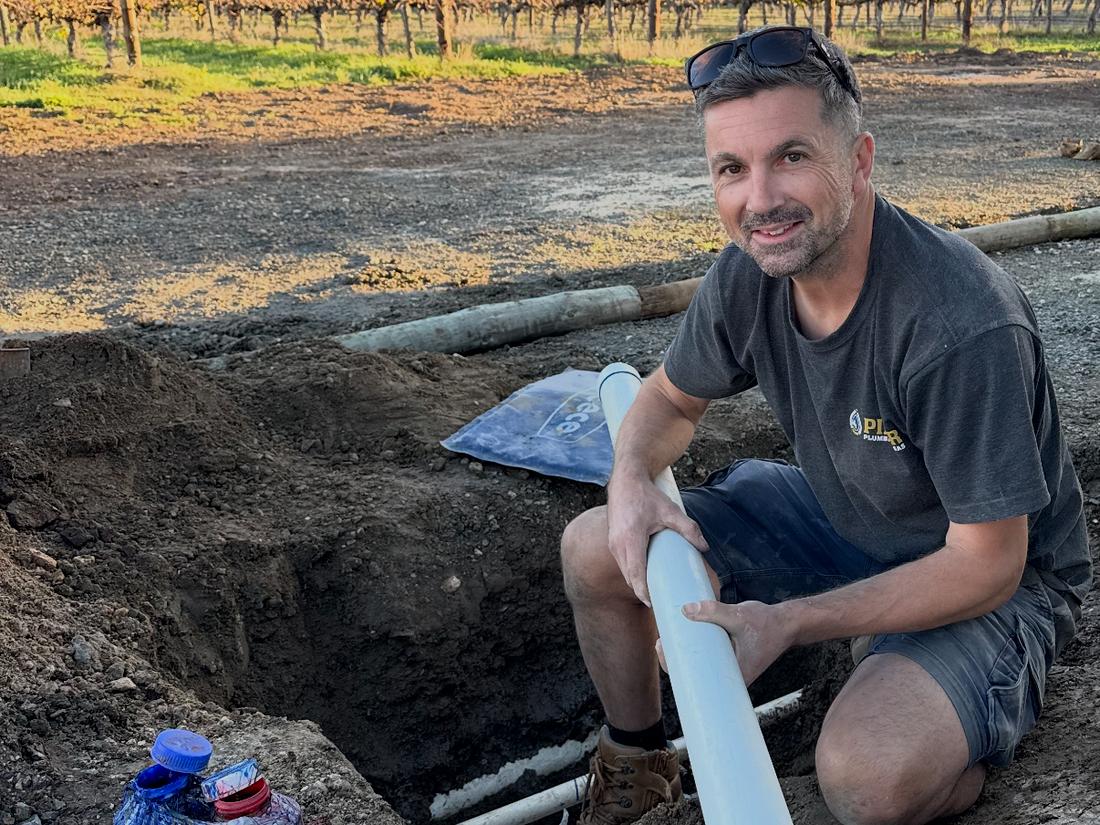 A new PVC line being laid in a trench beside a vineyard