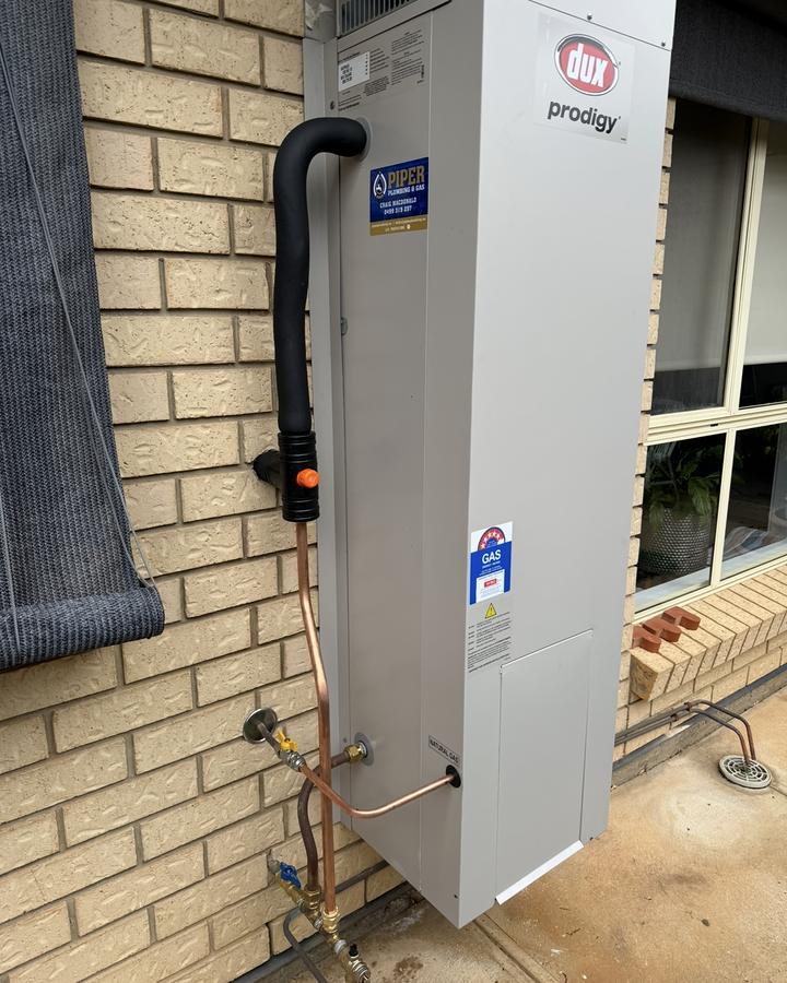 Gas storage hot water system on the side of a brick house