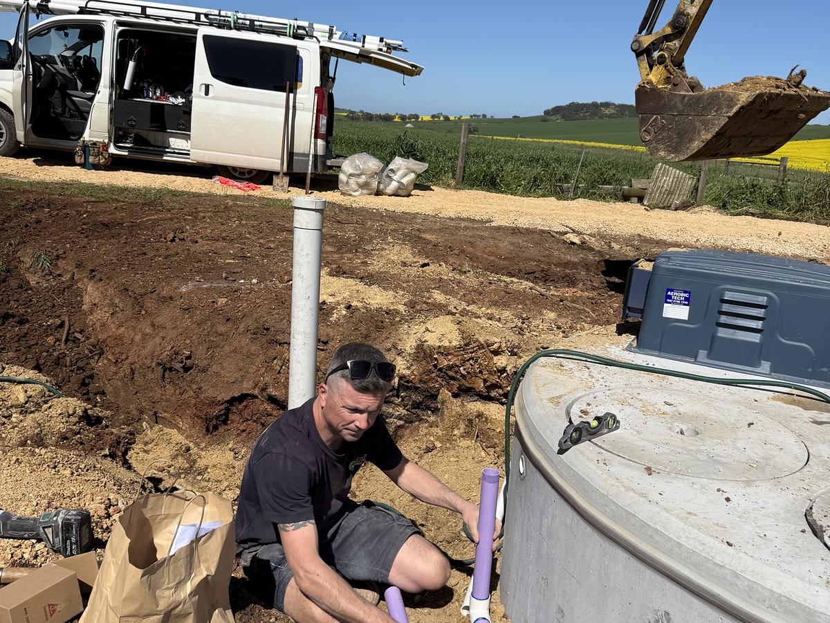 Craig plumbing in a new wastewater tank on a rural block, with the van and an excavator behind