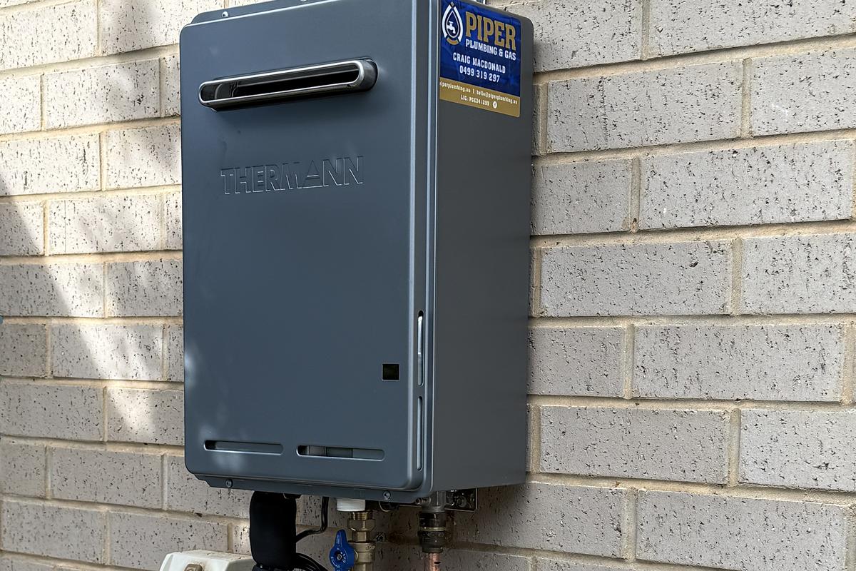 Continuous-flow gas hot water unit on a brick wall, with the Piper Plumbing & Gas sticker on it