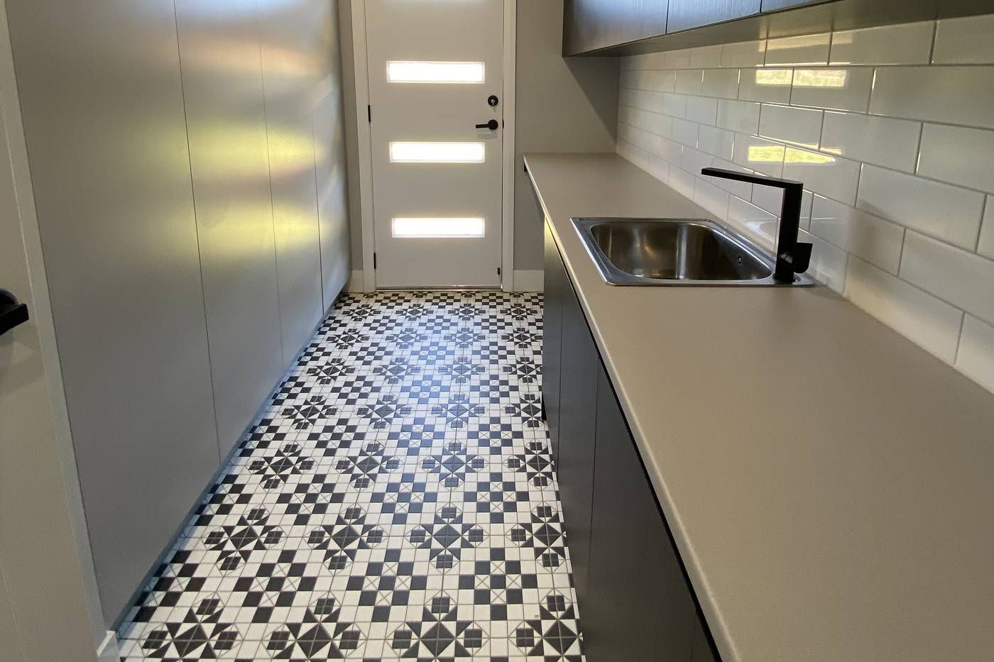 Renovated laundry with a long bench, black mixer and patterned floor tiles