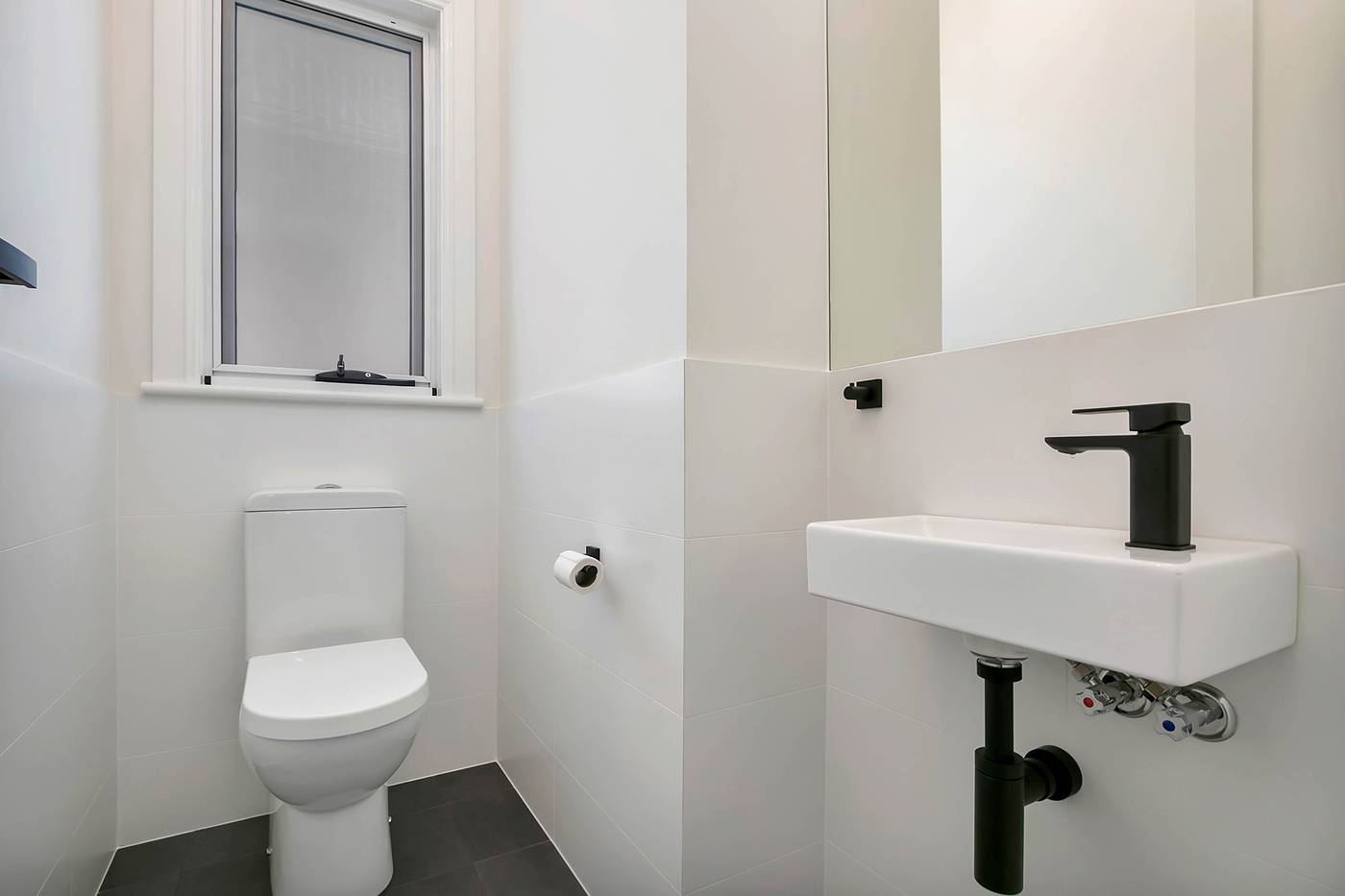 Powder room with a toilet and a wall-hung basin with black tapware