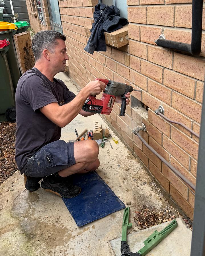 Craig drilling into the brick wall of a house to fit new copper water pipe
