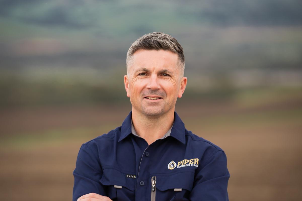 Craig from Piper Plumbing & Gas, arms crossed, in front of a Barossa paddock